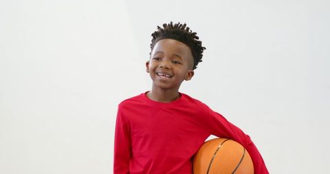 Smiling Boy in Red Holding Basketball Against White Background