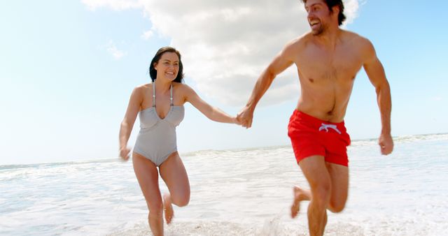 Happy caucasian couple holding hands and running on beach. Relationship, togetherness, summer, leisure, vacation and lifestyle, unaltered.