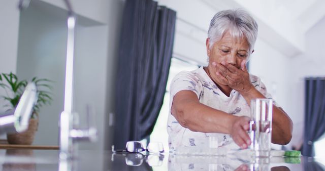Senior woman feeling unwell at home, reaching for medication on table. Frequent use for portraying elderly health concerns, home care situations, and senior healthcare. Ideal for healthcare articles, pharmacy promotions, and caregiving services.