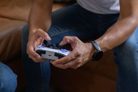 African man holding white-blue controller playing multiplayer game wearing smartwatch