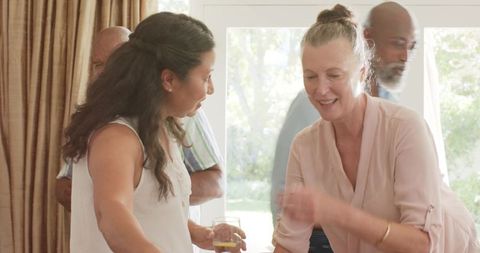 Mature women chatting and serving drinks during casual home gathering by sunlit doors