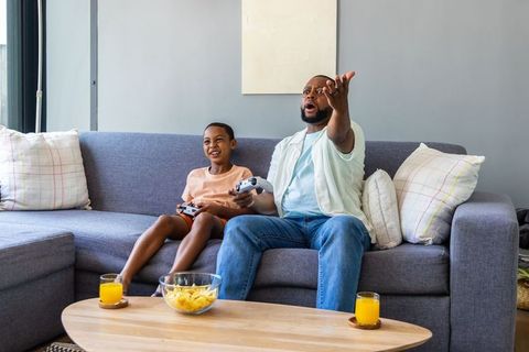 African american father and son playing video games and celebrating together on couch