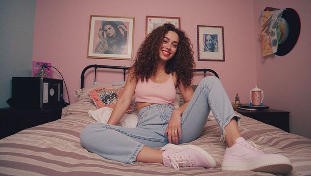 Trendy young woman relaxing in stylish pink bedroom with bohemian decor