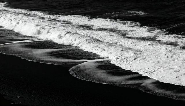 Crashing black sand waves creating high-contrast monochrome shoreline texture