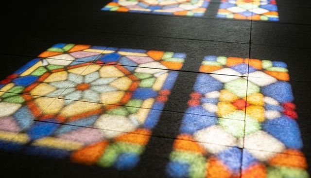 Projecting stained-glass light patterns across dark tiled floor with geometric rosettes