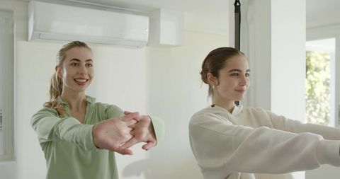 Two women stretching together in bright home studio wearing casual activewear for wellness