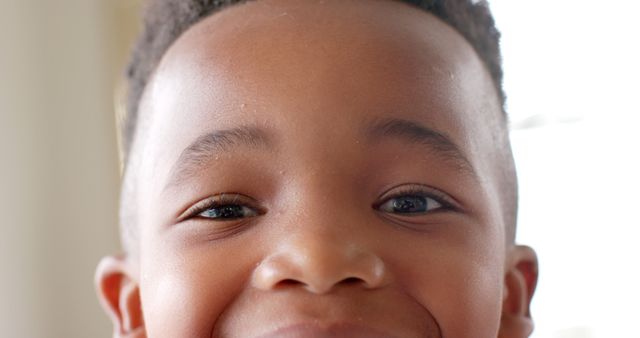 The close-up image of a young boy with afro hair smiling radiantly can be used for advertisements, educational resources, and promotional materials highlighting children's products, happiness, and inclusivity. Ideal for websites and blogs about parenting, childhood, and early education.