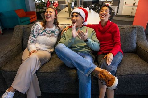 Coworkers laughing on office couch celebrating holiday spirit with santa hat and antlers