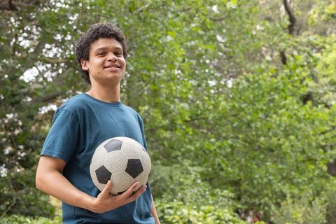 Young man holding soccer ball standing in green park smiling athlete enjoying outdoors