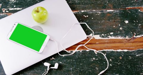 Smartphone with green screen and earphones on rustic wooden table
