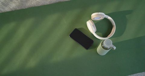 Minimal yoga essentials resting on emerald mat with headphones phone water bottle