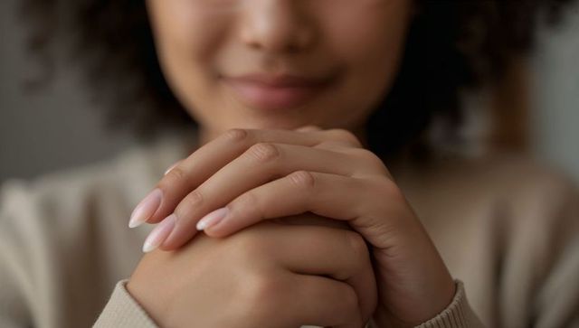 Curly-haired woman clasping hands, manicured nails warm soft-focus closeup portrait
