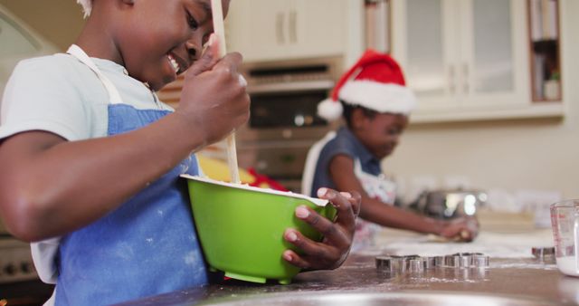 Two children are in the kitchen baking cookies, creating holiday memories. One child is stirring a mixing bowl while the other is using cookie cutters to shape dough, reflecting joyful and warm interaction. Ideal for use in advertisements, holiday greeting cards, baking, and family-related promotional materials.