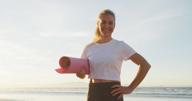 Portrait of caucasian woman holding yoga mat at the beach smiling. healthy active lifestyle, outdoor fitness and wellbeing.