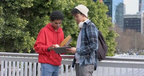 Multicultural college students collaborating on tablet outdoors near urban campus