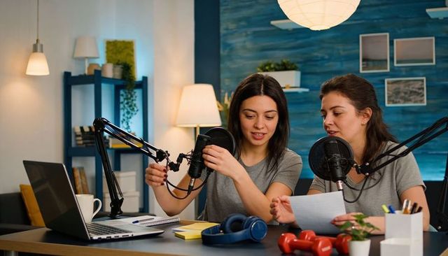 Female podcast hosts recording and adjusting microphones in cozy home studio