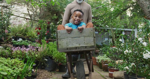 Father pushing his son in a wheelbarrow filled with plants at a garden center. The boy is smiling and enjoying the ride. This depiction of family bonding and joy in nature can be used for articles or advertisements about family activities, outdoor gardening, and environmental education.