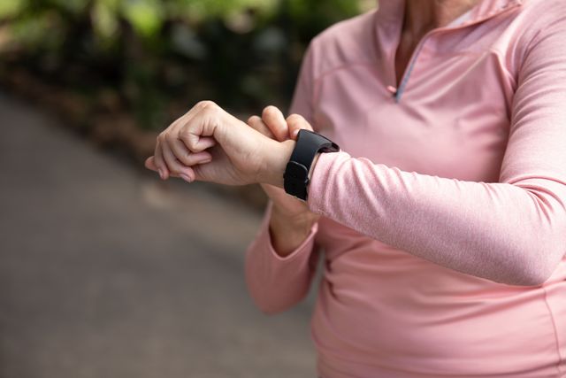 Mid section of senior Caucasian woman working out in the park wearing sports clothes, checking her smartwatch. Retirement healthy lifestyle activity.