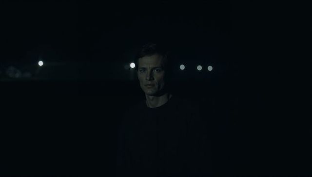 Solitary man standing in deep night with distant lamp bokeh, moody low-key portrait