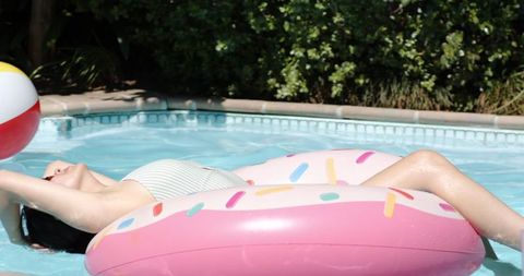 Woman floating on inflatable in pool reaching for beach ball