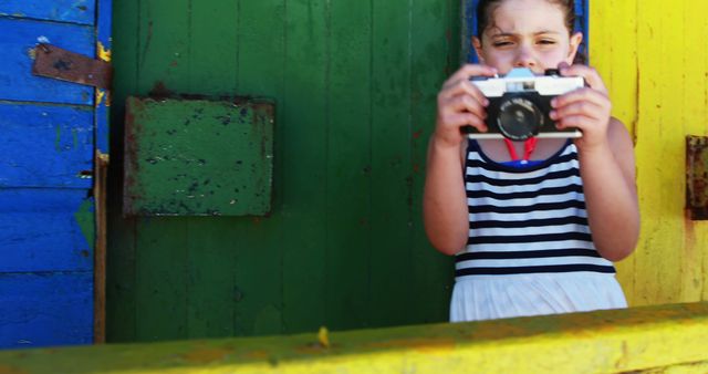 A young Caucasian girl takes a photo with a vintage camera against a colorful backdrop, with copy space. Her playful curiosity is captured in this vibrant setting, emphasizing a moment of creativity and exploration.