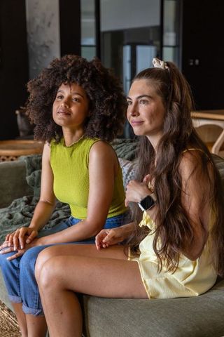 Diverse friends sitting on sofa wearing smartwatch and scrunchie, cozy living room moment