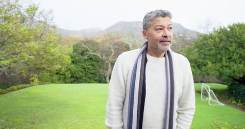 Mature man enjoying peaceful garden stroll wearing knit sweater and striped scarf
