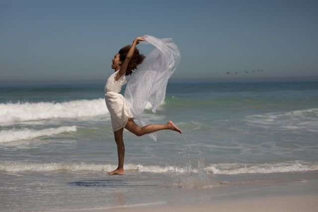 African American woman running on a beach, arms outstretched, lifting the train of her dress. Free time and vacation.