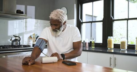 Man measuring blood pressure in modern kitchen for health monitoring