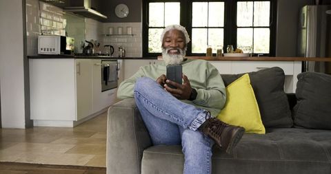 Senior man relaxing with smartphone on stylish sofa at home
