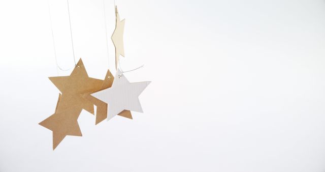 Minimalist image featuring paper stars hanging against a white background. Ideal for use in holiday cards, decorations, minimalist design projects, or DIY craft tutorials. The image's simplicity complements themes like creativity, holidays, and modern décor.