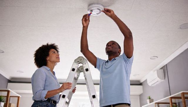 Couple installing smoke detector in living room using ladder for home safety