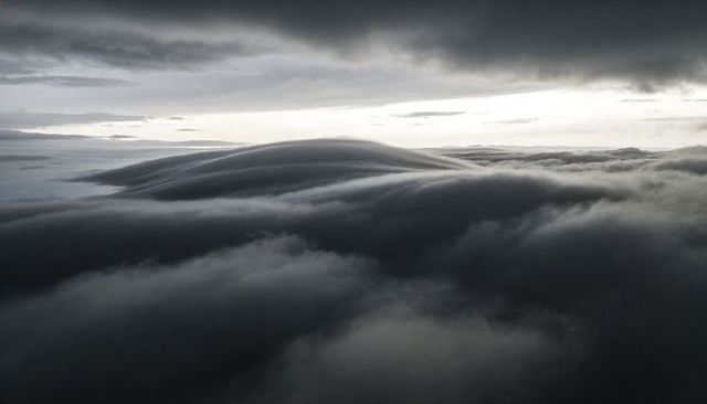 Rolling dome cloud formation over layered sky, dramatic monochrome aerial landscape
