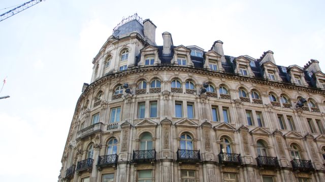 The ornate facade of an old European building showcases classic architectural detailing with numerous windows and a curved balcony. Ideal for use in travel content, urban design articles, or historical architecture references.