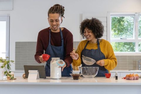 African american couple baking together in modern kitchen using tablet and measuring flour
