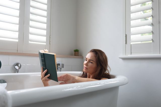 Beautiful woman reading a book while relaxing in bathtub at bathroom