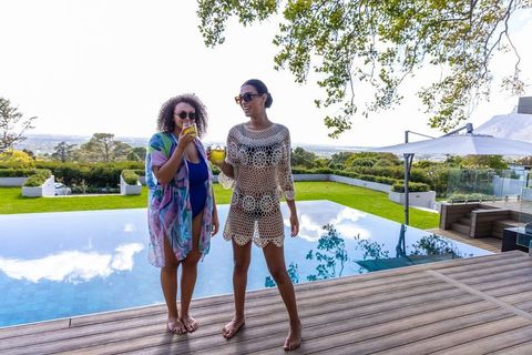 African american women enjoying drinks at infinity pool on luxury coastal terrace