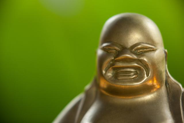This image features a close-up of a gold painted Laughing Buddha figurine against a green background. It can be used in articles or websites related to spirituality, Buddhism, meditation, and Asian culture. It is also suitable for use in decorative and home decor contexts, as well as for promoting concepts of happiness and prosperity.