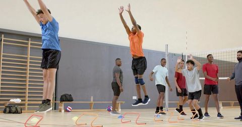 Teen volleyball training in gymnasium performing jumping spiking drills and agility hurdles