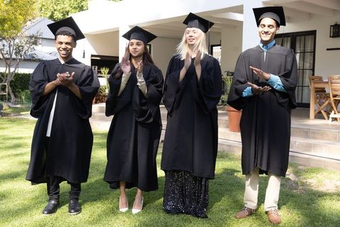 Diverse friends celebrating graduation in black gowns outdoor