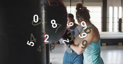 Female boxer training with coach guiding heavy bag in modern gym with numeric overlay