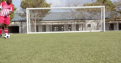 Athlete Dribbling Soccer Ball Near Goal on Green Field