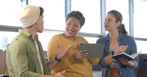 Diverse team collaborating in modern workspace using tablet and notebook for brainstorming