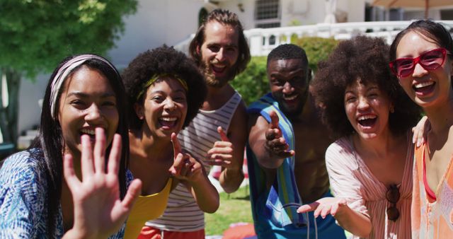 Portrait of diverse group of friends smiling and waving to camera at a pool party. Hanging out and relaxing outdoors in summer.