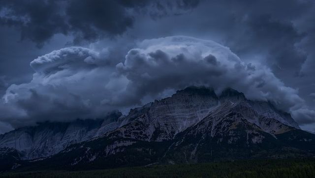 Anvil cloud looming over jagged alpine massif with lightning at moody twilight
