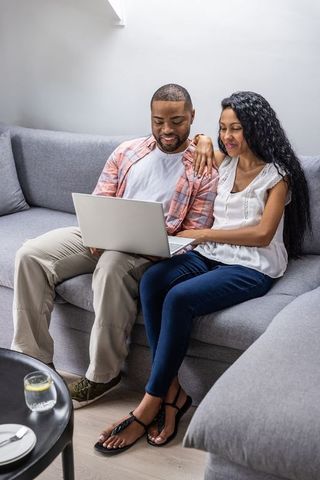 Couple sharing laptop on grey sofa, cozy living room moment for home life and planning