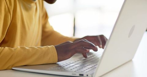 Young african man typing on laptop at bright desk, close-up hands on keyboard, remote work