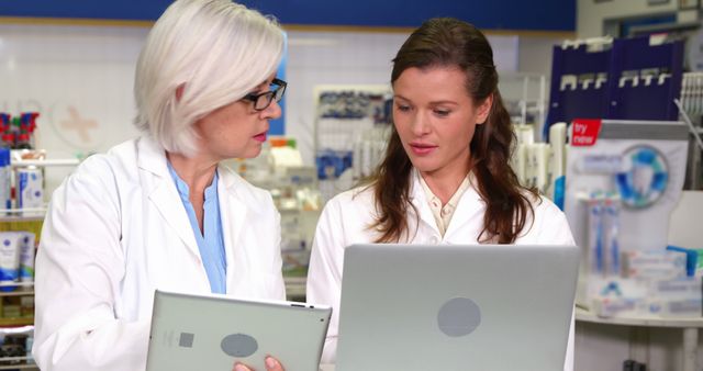 Two female pharmacists using tablets to discuss prescriptions in a modern pharmacy. Ideal for health IT services, pharmacy technology advertisements, healthcare teamwork visuals, or modern healthcare marketing.