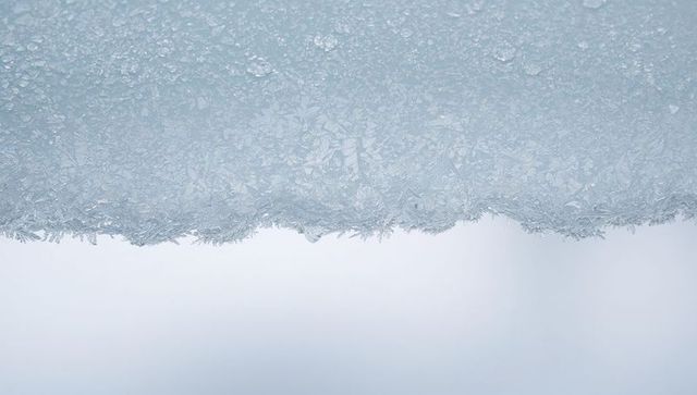 Delicate ice fringe with hanging droplet and crystalline needles on frosted ledge close-up