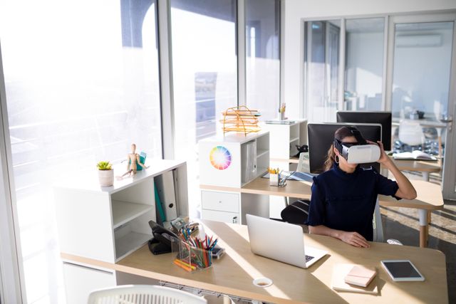 Female executive using virtual reality headset at her desk in a modern office. Ideal for illustrating concepts of technology in the workplace, innovation, and the integration of VR in business environments. Useful for articles, blogs, and presentations on modern office trends, tech advancements, and professional settings.
